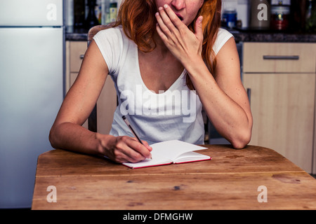 Tired young woman taking notes in her kitchen Stock Photo