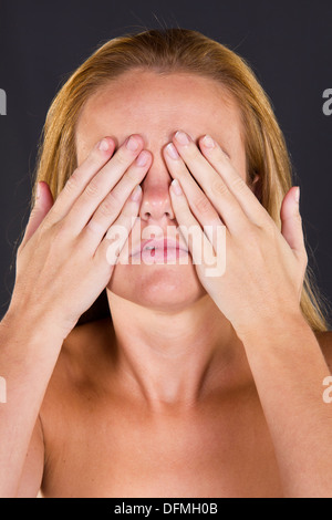 A young woman covering her eyes with her hands The three wise monkeys.  See no evil, see no evil, speak no evil Stock Photo