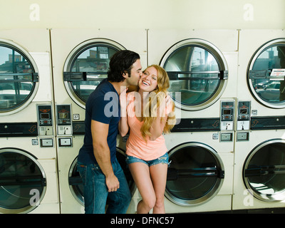 A young man kisses on the chick of a pretty woman in San Diego coin laundromat. Stock Photo