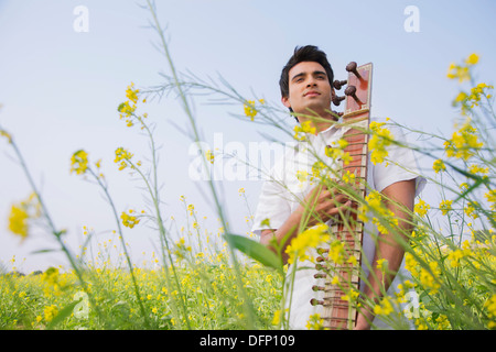 Low angle view of a man playing sitar in a mustard field Stock Photo