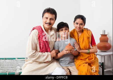 Portrait of a couple sitting with their son holding a piggy bank Stock Photo