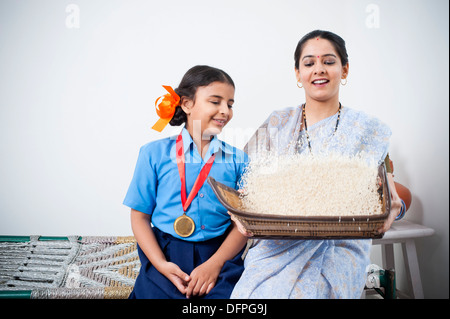 Girl sitting beside her mother winnowing rice in a basket Stock Photo