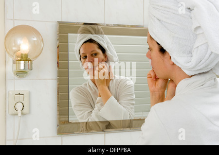 A woman is depilating the small hairs from her mustache in front of a mirror Stock Photo