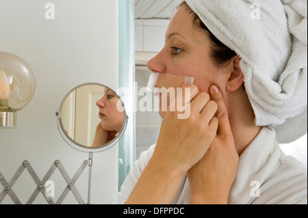 A woman is depilating the small hairs from her mustache in front of a mirror Stock Photo