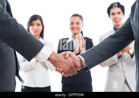 Two businessmen shaking hands with their colleagues applauding Stock Photo