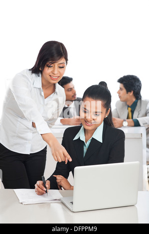 Two businesswomen working in the office with their colleagues in the background Stock Photo
