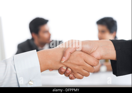 Two businesswomen shaking hands with their colleagues in the background Stock Photo