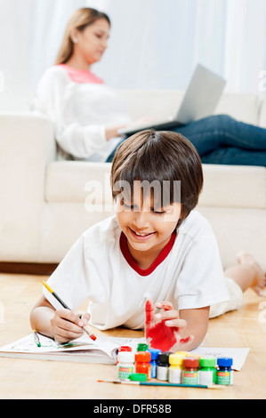 Boy making a painting with his mother using laptop in the background Stock Photo