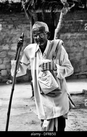 Old Indian man with walking stick going to Sri Sathya Sai Baba mobile outreach hospital. Andhra Pradesh, India. Monochrome Stock Photo