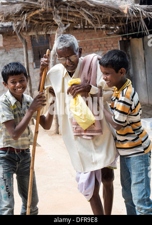 Two Indian boys helping an old Indian man with walking stick at Sri Sathya Sai Baba mobile outreach hospital. India Stock Photo