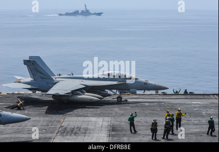 An F/A-18F Super Hornet assigned to the Black Knights of Strike Fighter Squadron (VFA) 154 prepares to launch off the flight deck aboard the aircraft carrier USS Nimitz (CVN 68) while the guided-missile destroyer USS Stockdale (DDG 106) sails in the backg Stock Photo