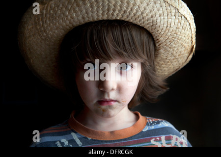 Four and a half year old boy wearing a wicker hat and looking serious. Stock Photo
