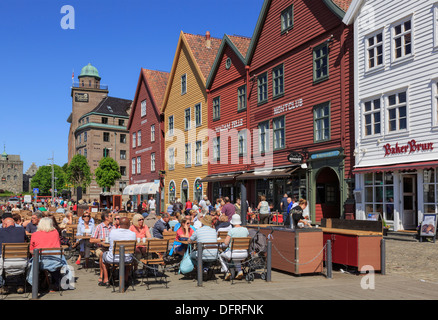 Tourists dining outside in restaurants on waterfront by Bergen's historic 14th century wooden buildings in summer on Bryggen, Bergen Hordaland Norway Stock Photo