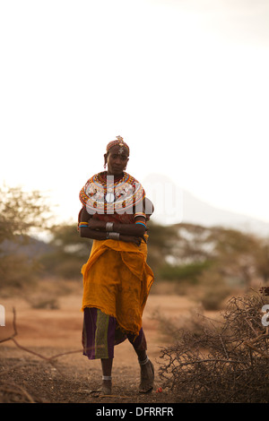 A Rendille woman holding her baby on her back walks into her village, near Laisamis, Kenya Stock Photo