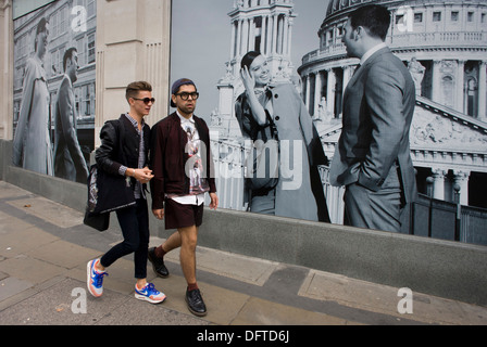 Two men walk past a fashion poster showing a fashion boy and girl and St Paul's Cathedral. Stock Photo