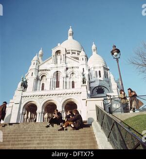 Young people sit on the stairs in front of the Sacre Coeur de Montmartre in Paris, France, in November 1970. The basilica is located on the hill of Montmartre. Photo: Wilfried Glienke Stock Photo