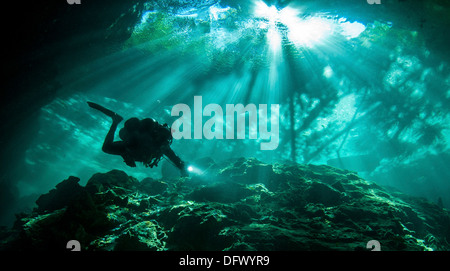 Diver passes through light beams in Chac Mool cenote in Mexico. Stock Photo