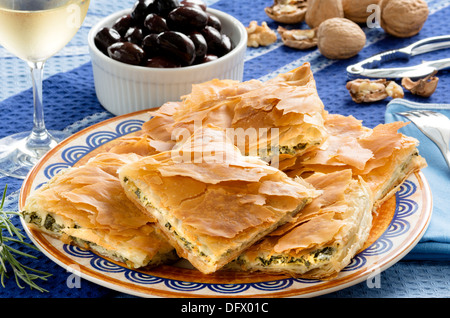 Spanakopita, Greek spinach pie with feta cheese and filo party on on plate with Greek white wine, olives and walnuts Stock Photo