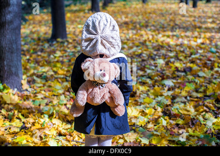 Rear view of charming little girl with a backpack-bear behind in the autumn sunny forest Stock Photo