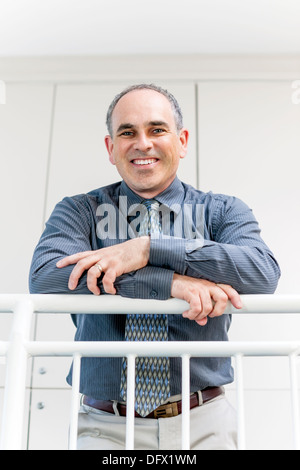 Portrait of smiling proud business man standing in office hallway leaning on railing Stock Photo