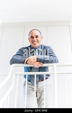 Smiling proud business man standing in office hallway leaning on railing Stock Photo