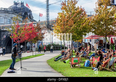 Autumn in Berlin - people sit on deckchairs at Spree riverside listening to music of street entertainer Stock Photo