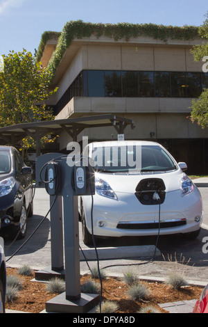 Plug-in electric cars plugged into an EV charging station to charge their batteries in a workplace parking lot Stock Photo