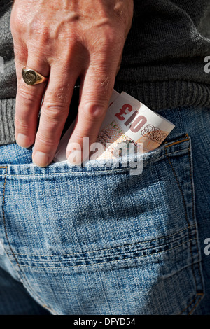 Close up of person man putting English cash banknote £10 ten pound pounds notes money in jeans back pocket England UK United Kingdom Great Britain Stock Photo