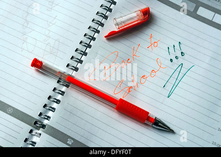 Notebook with metal spiral and pencil, opened at one page that says BACK TO SCHOOL in colors green and orange. Stock Photo