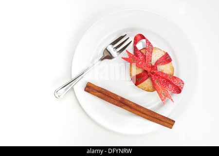 Sweet Christmas mince pieand cinnamon stick with a red ribbon tied round it on a White plate and background. Stock Photo