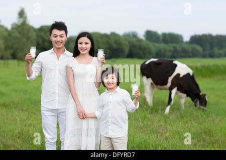 Happy family holding glasses of milk with cattle grazing in the pasture Stock Photo