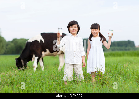 Happy children holding glasses of milk with cattle grazing in the pasture Stock Photo