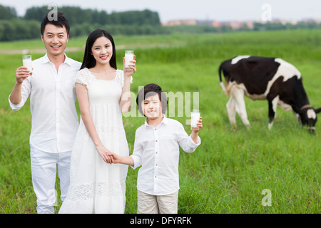 Happy family holding glasses of milk with cattle grazing in the pasture Stock Photo