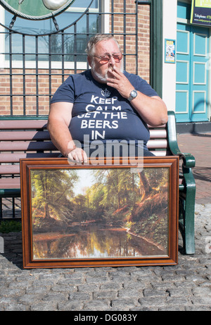 Obese man smoking and holding painting Gosport, Hampshire, England, UK Stock Photo