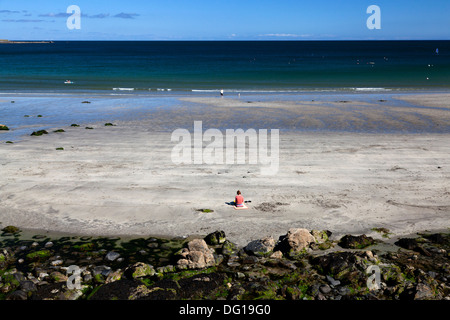 Solitary woman sitting on the beach, Coverack, Cornwall Stock Photo