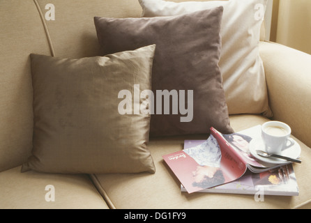 Close-up of brown and beige silk cushions with cup of coffee and magazines on cream sofa Stock Photo