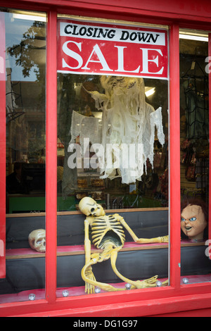 A shop window with closing down sale sign in the window and a joke skeleton on display Stock Photo