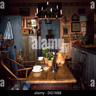Candles in metal chandelier above antique wooden table and stick-back chairs in dark cottage kitchen Stock Photo
