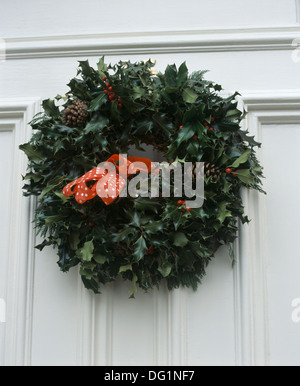 Close-up of Christmas holly wreath tied with red ribbon on front door Stock Photo