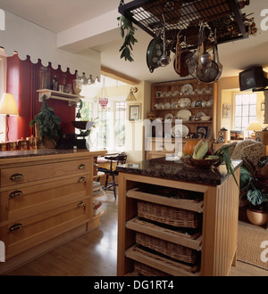 Pans on storage rack above island unit with wicker storage baskets on shelves in country kitchen Stock Photo