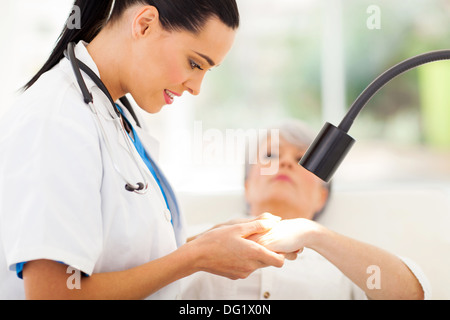 friendly dermatologist examining senior woman's skin under light Stock Photo