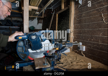 A sliding compound mitre saw, in a workshop, cutting timber with sawdust being ejected from the rear of the saw. Stock Photo