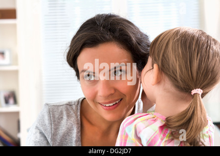 Happy mother with her daughter saying a secret in doors Stock Photo