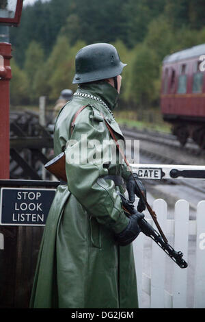 1940 Wartime army man, an Armed railway guard  wearing coat, and tin hat in Levisham. North Yorkshire, UK. German Station Guards or Feldgendarmerie at the  ‘Railway in Wartime’  North Yorks Moors Railway (NYMR) event at Levisham Railway Station in inclement weather on weekend 12th-13th October 2013.   Levisham Station, was decorated with period posters, and French signs  during the (NYMR) ‘Wartime Weekend’ to become  ‘Le Visham’ in northern France. The gathering, a recreation of a French village occupied by World War Two, World War II, Second World War,  WWII, WW2 German troops. Stock Photo