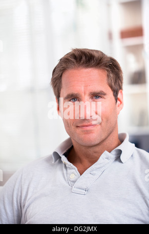 Male Sitting On Sofa Relaxing At Home Looking To Camera Smiling Stock Photo
