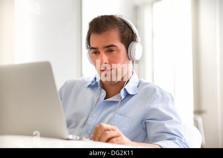 Man listening to music with earphones on laptop computer, sitting on sofa