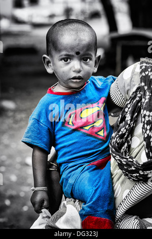 Poor Indian low caste child wearing a superman t shirt carried by his mum. Andhra Pradesh, India. Monochrome and spot coloured. Stock Photo