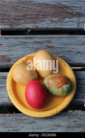 Shabby chic Easter, a bowl of eggs ,. Old yellow vintage pottery dish holding four painted multi colored Easter eggs Stock Photo