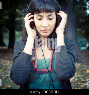 young beautiful woman listening to music at the park in autumn Stock Photo