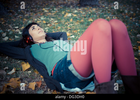 young beautiful woman listening to music at the park in autumn Stock Photo